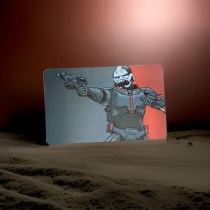 May include: Illustration of a character in a black and gray suit, holding a blaster pistol. The character has a white helmet with black accents and a red and black background. The image is set against a brown, textured surface.