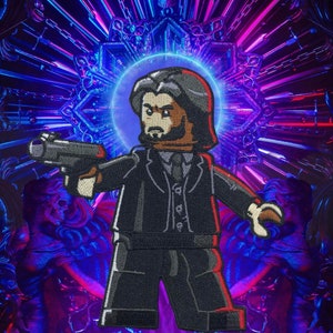 May include: A black and gray embroidered patch of a Lego minifigure holding a gun. The minifigure is wearing a black suit, white shirt, and black tie. The background is a blurry image of a neon light display.