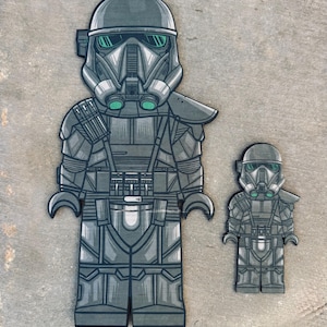 May include: Two black and green Star Wars Stormtrooper LEGO minifigures. The larger figure is standing and the smaller figure is standing. Both figures have detailed helmets and armor.