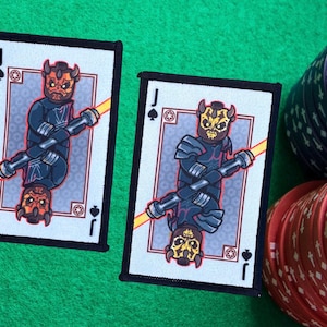 Pode incluir: Dois baralhos de cartas com os personagens de Star Wars Darth Maul e o General Grievous. Os baralhos são ambos Valetes de Paus e estão em uma moldura preta.