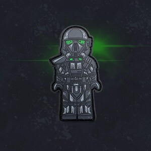 May include: A black and green detailed Lego-style figure of a Star Wars Stormtrooper with a green visor.