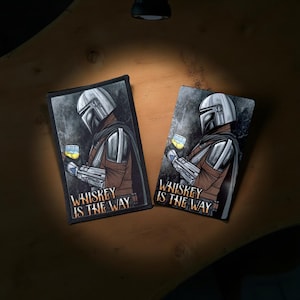 May include: Two rectangular patches featuring a character in a helmet holding a glass of whiskey. The patches have a dark background with the text "Whiskey Is The Way" in white. The character is wearing a silver helmet and brown armor.
