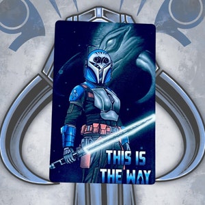 May include: A blue and gray Mandalorian with a lightsaber and the text "This is the way" on a black background.