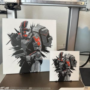 May include: Two prints of a Star Wars character, a clone trooper, in a black and red suit with a white background. The larger print is 8x10 inches and the smaller print is 4x6 inches.