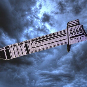 May include: A silver-colored metal pin shaped like a spaceship with a detailed design. The pin has a black and white pattern and a small window on the top.