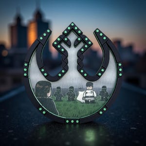 Op de afbeelding: Een zwart en zilver embleem met een gestileerd ontwerp en groene accenten. Het embleem heeft een centraal beeld van Lego-achtige figuren op een grasveld. De achtergrond toont een stadsgezicht in de schemering.