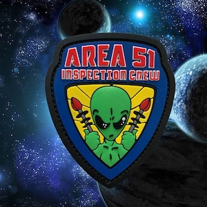 May include: A patch with the words "AREA 51 INSPECTION CREW" in red and white lettering. The patch features a green alien holding two red and black tools. The patch is blue, yellow, and black, with a space-themed background.