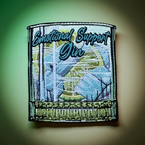 May include: Embroidered patch featuring a cocktail glass filled with ice cubes and a lime wedge. The patch reads "Emotional Support Gin" in a teal script font. The patch has a black border and a green fringe.