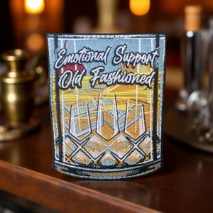 May include: Embroidered patch with the text "Emotional Support Old Fashioned" in white script. The patch features a design of three cocktail glasses with a yellow and blue background. The patch has a black border.