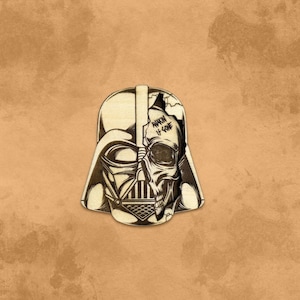 May include: A wooden cutout of Darth Vader's helmet with a skull design on the right side. The skull has the words "ANAKIN IS GONE" written on it.