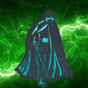 May include: A black and teal embroidered patch depicting a hooded figure holding a sword. The figure is standing on a green background.