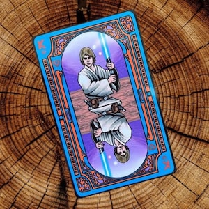 Op de afbeelding: Een speelkaart met een blauwe en oranje rand. De kaart toont een portret van Luke Skywalker uit Star Wars, die een lightsaber vasthoudt. De kaart is een Koning van harten.