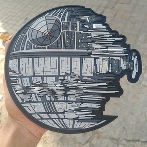 May include: A black and gray Death Star patch with a detailed design. The patch is made of a textured material and has a slightly worn look.