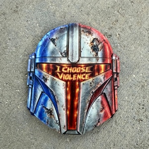 May include: A helmet with a weathered metallic finish featuring blue shading on the left and red shading on the right. The visor displays the text I CHOOSE VIOLENCE in glowing orange letters against a dark background with a vertical orange light.