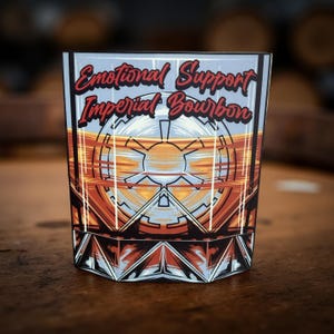 May include: A square-shaped rocks glass with the words "Emotional Support Imperial Bourbon" in red script. The glass features a geometric design in orange, black, and white, with a light blue background. The glass is likely for bourbon or whiskey.