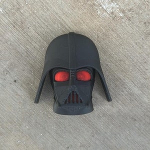 Könnte beinhalten: Ein schwarzer Darth-Vader-Kopf aus Kunststoff mit roten Augen. Der Kopf ist ein 3D-gedrucktes Modell.