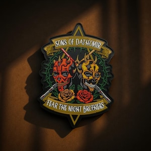 Pode incluir: Um patch preto com duas caveiras estilizadas, uma vermelha e outra amarela, com armas semelhantes a sabres de luz. O patch diz "SONS OF DATHOMIR" e "FEAR THE NIGHT BROTHERS" com rosas e uma coroa de espinhos.