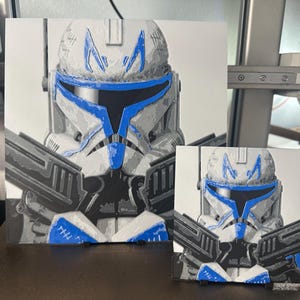 May include: Two framed prints of a Star Wars clone trooper with a blue and white helmet. The larger print is a close-up of the helmet, while the smaller print shows the trooper's full body.