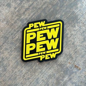 Pode incluir: Adesivo preto e amarelo com a palavra "PEW" repetida três vezes em um design empilhado.
