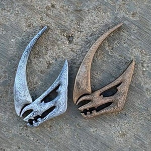 May include: Two Mandalorian symbol pendants, one silver and one gold, with a textured finish.