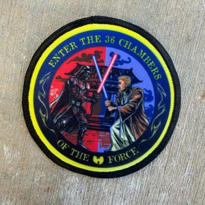 May include: A circular embroidered patch featuring a split red and blue background with a black-clad figure and a robed figure dueling with light-up swords. The text ENTER THE 36 CHAMBERS OF THE FORCE is printed in yellow along the border.