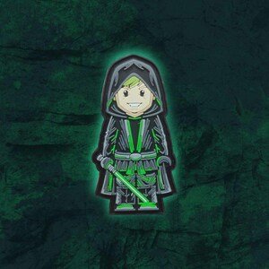 May include: A cartoon-style character in a black hooded robe with green accents and a green lightsaber. The character has a smiling face and is set against a dark green, textured background. The design has a glowing green outline.