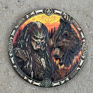 May include: A circular wooden plaque featuring a detailed relief carving of a Predator creature standing next to a bear head. The background displays a forest scene with a sunset sky in orange and red hues. The border is decorated with bone-like shapes.