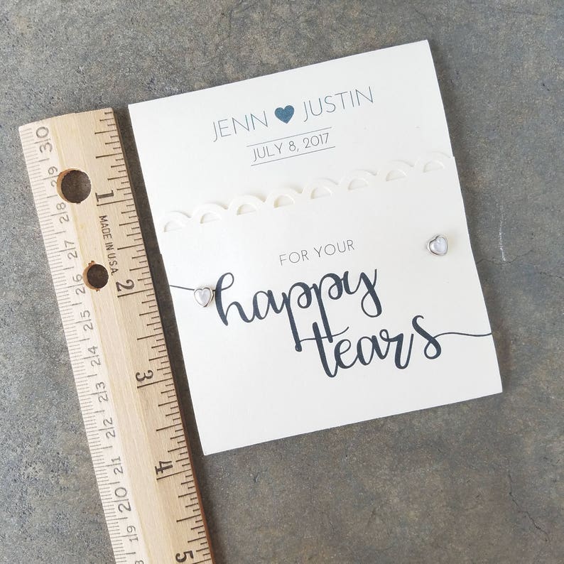 May include: A white card with a decorative border and the text "JENN JUSTIN JULY 8, 2017" and "FOR YOUR happy tears". Two small silver heart-shaped charms are attached to the card.