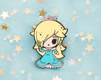 Puede incluir: Un pin de esmalte de color dorado que representa una caricatura de la princesa Rosalina de la franquicia Super Mario. Lleva un vestido azul y una corona, y sostiene una varita con forma de estrella.