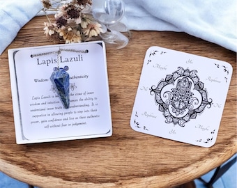 Puede incluir: Un péndulo de lapislázuli azul en una cadena plateada dentro de una caja blanca con el texto Lapis Lazuli Wisdom-Authenticity, junto a una tarjeta cuadrada blanca con una ilustración negra de una mano de Hamsa y las palabras Yes, No, Maybe.