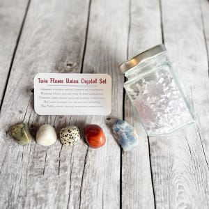 May include: A Twin Flame Union Crystal Set with a variety of stones, including a white Moonstone, a red Jasper, and a blue Calcite. A glass jar filled with white confetti sits next to the crystals. A card with text is also present.