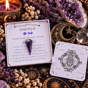 May include: A faceted purple amethyst crystal pendulum on a silver chain, presented in a white box with text describing its properties. Beside it lies a square white card featuring a black hamsa hand illustration and the words Yes, No, Maybe, Rephrase.