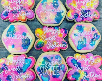 May include: A set of nine decorated sugar cookies with colorful frosting and gold glitter. The cookies are decorated with the words "Happy Sweet Sixteen" and "Maddison".