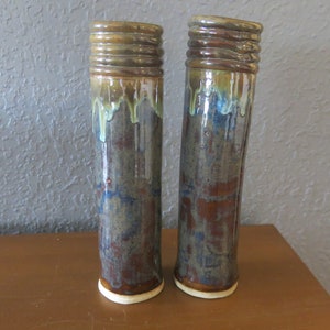 Puede incluir: Dos jarrones de cerámica con un esmalte marrón, azul y verde. Los jarrones tienen una forma cilíndrica con una parte superior ligeramente acampanada.