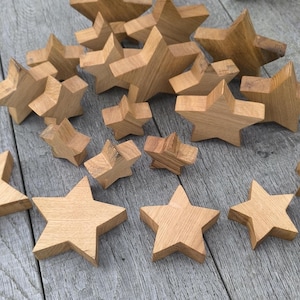Könnte beinhalten: Eine Sammlung von Holzsternen in verschiedenen Größen, alle in natürlicher Holzfarbe. Die Sterne sind in einem zufälligen Muster auf einer grauen Holzoberfläche angeordnet.