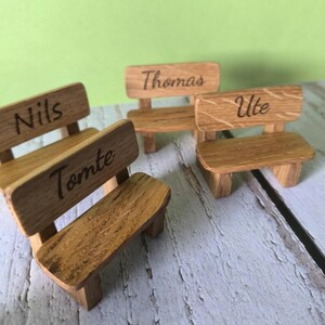 Könnte beinhalten: Vier Miniatur-Holzbänke mit personalisierten Namen: Nils, Tomte, Thomas und Ulte. Die Bänke sind aus hellbraunem Holz gefertigt und haben eine rustikale Oberfläche.
