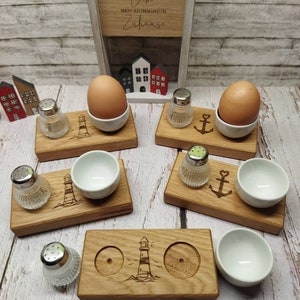 Könnte beinhalten: Frühstücks-Set aus Holz mit Leuchtturm-Design, einschließlich Eierbecher, Salzstreuer und kleinen Schalen. Das Set hat eine natürliche Holzoberfläche und ein maritimes Thema. Der Text auf dem Holzschild lautet "Liebe macht aus einem Hafen Zuhause."