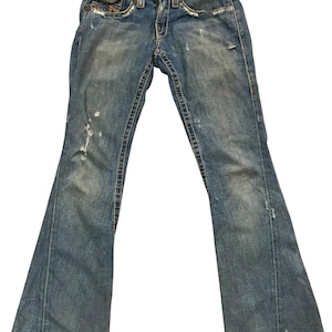 May include: Blue denim jeans featuring a distressed finish with faded areas, frayed edges, and visible stitching. These jeans have a classic five-pocket design, a button and zipper fly closure, and a flared leg silhouette with a medium wash.