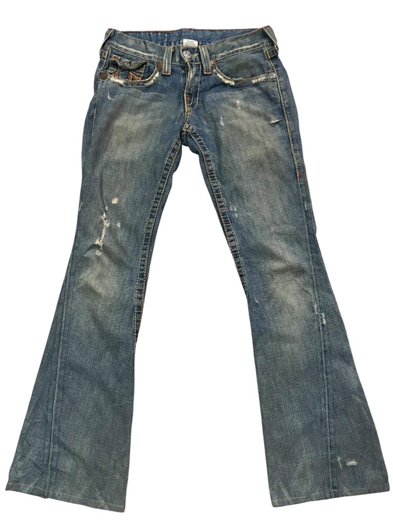 May include: Blue denim jeans featuring a distressed finish with faded areas, frayed edges, and visible stitching. These jeans have a classic five-pocket design, a button and zipper fly closure, and a flared leg silhouette with a medium wash.