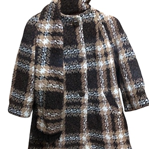 Puede incluir: Un abrigo a cuadros marrón, blanco y negro con cuello alto y mangas tres cuartos. El abrigo tiene dos bolsillos delanteros y cierre de botones. La tela tiene una apariencia texturizada.