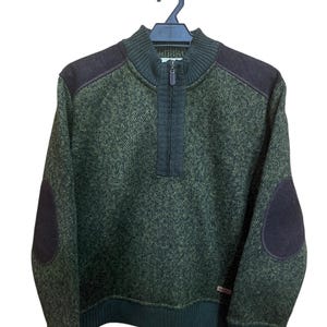 May include: Green and brown textured sweater with a quarter-zip closure. The sweater features dark brown shoulder patches and elbow patches. The collar, cuffs, and hem are a darker shade of green. The sweater is hanging on a black hanger.