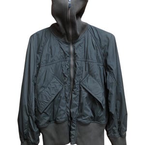 May include: Dark olive green bomber jacket with a high, ribbed collar and cuffs. The jacket features a full zip and two front pockets. The fabric has a slight sheen, and the design is minimalist and modern.