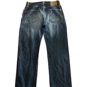 May include: Faded blue denim jeans with a classic five-pocket design. The jeans feature a straight leg cut and a leather patch on the back waistband. The back pockets have a decorative stitching pattern.