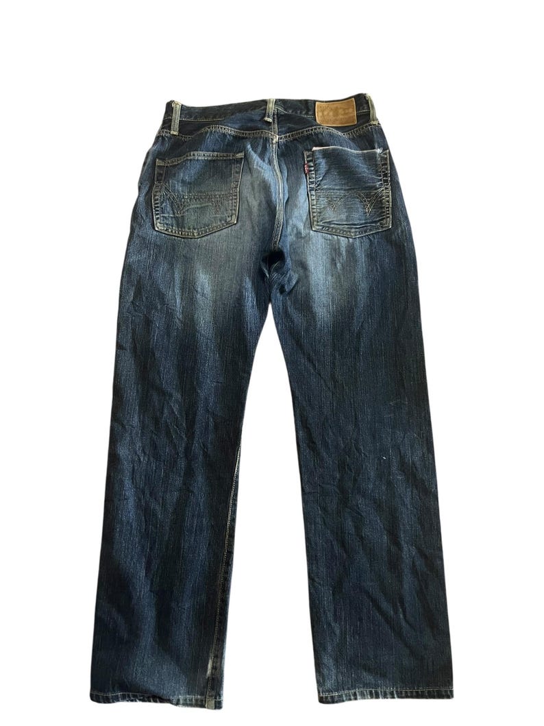May include: Faded blue denim jeans with a classic five-pocket design. The jeans feature a straight leg cut and a leather patch on the back waistband. The back pockets have a decorative stitching pattern.