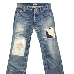 Könnte beinhalten: Blaue Jeans mit Distressed-Patches. Die Jeans haben einen Knopfverschluss und mehrere Patches unterschiedlicher Größe und Textur. Einige Patches weisen Distressed-Details auf, und die Jeans weisen Gebrauchsspuren auf.