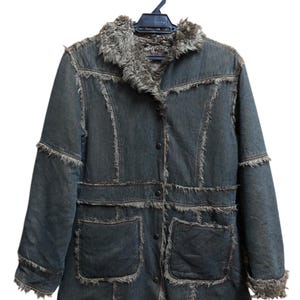 May include: A denim jacket with a faux fur collar and trim, hanging on a black hanger. The jacket has a button-up front, two front pockets, and frayed edges. The jacket is a dark blue color.