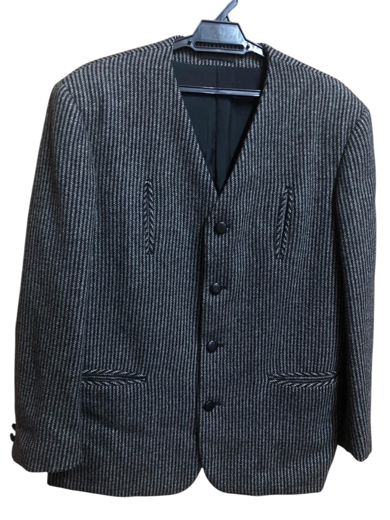 May include: A dark gray and brown striped blazer with a V-neck and four black buttons. The blazer has two front pockets and decorative stitching details. It is hanging on a black hanger.