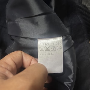 May include: A close-up of a black garment's interior, revealing a tag with the text "ECDAN-41360" and care symbols. The fabric appears to be a dark, possibly velvet or satin material.