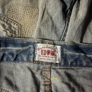 K&ouml;nnte beinhalten: Nahaufnahme einer blauen Jeans mit einem sichtbaren Patch und dem Markenetikett "EDWIN". Auf dem Etikett steht "Genuine Quality Jeans" und "Exclusive design for lasting good look".