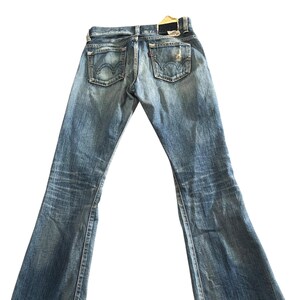 May include: Faded blue denim jeans with a flared leg design. The jeans feature classic five-pocket styling, a distressed look, and a leather patch on the back. The jeans are a vintage style.